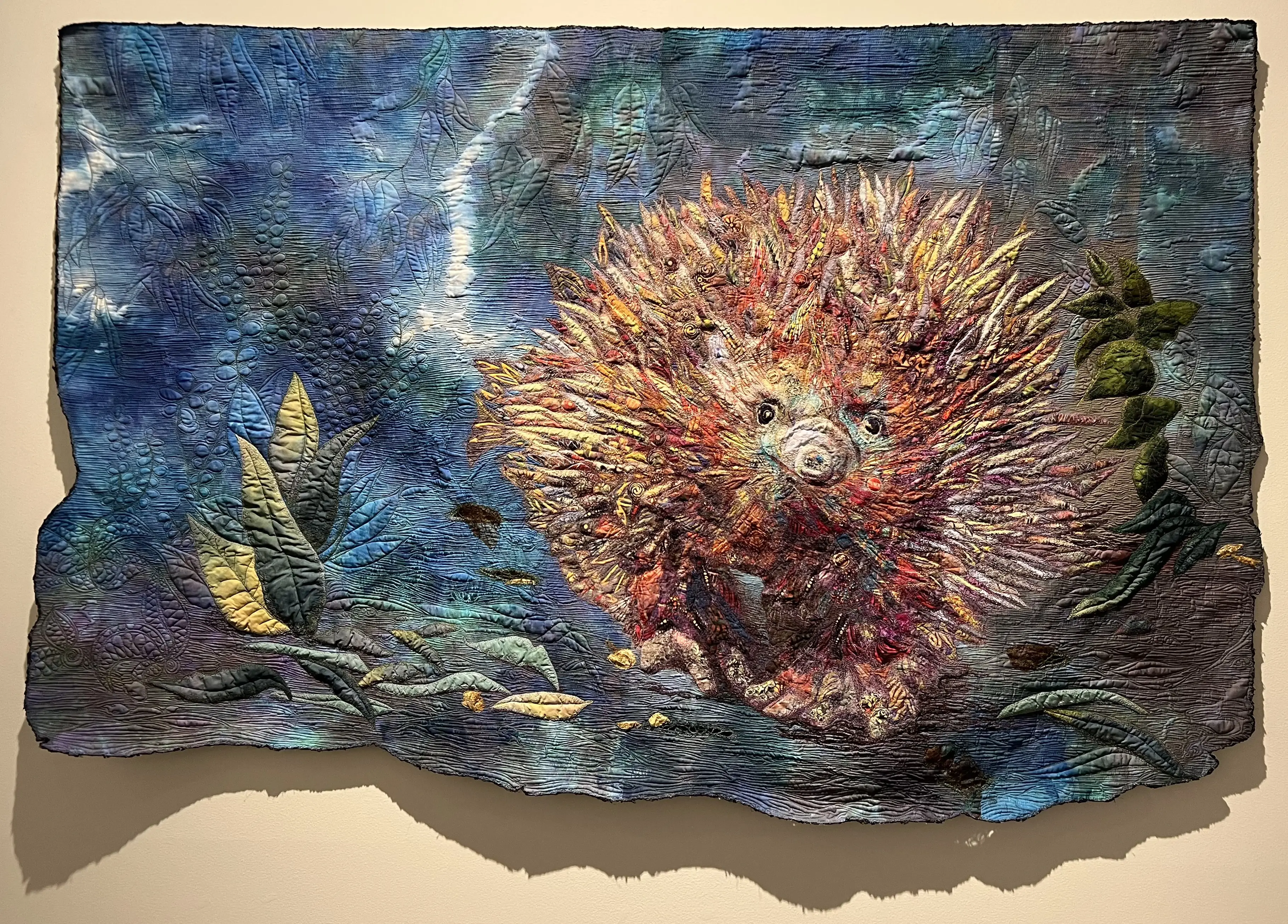 Sue de Vanny, 'Unguarded Moment', 2024. A collage of cotton fabrics: commercial printed fabrics and hand-dyed fabric on a hand-dyed background. Free motion thread painting and quilting. Yarn couched edging. 109 x 166cm.